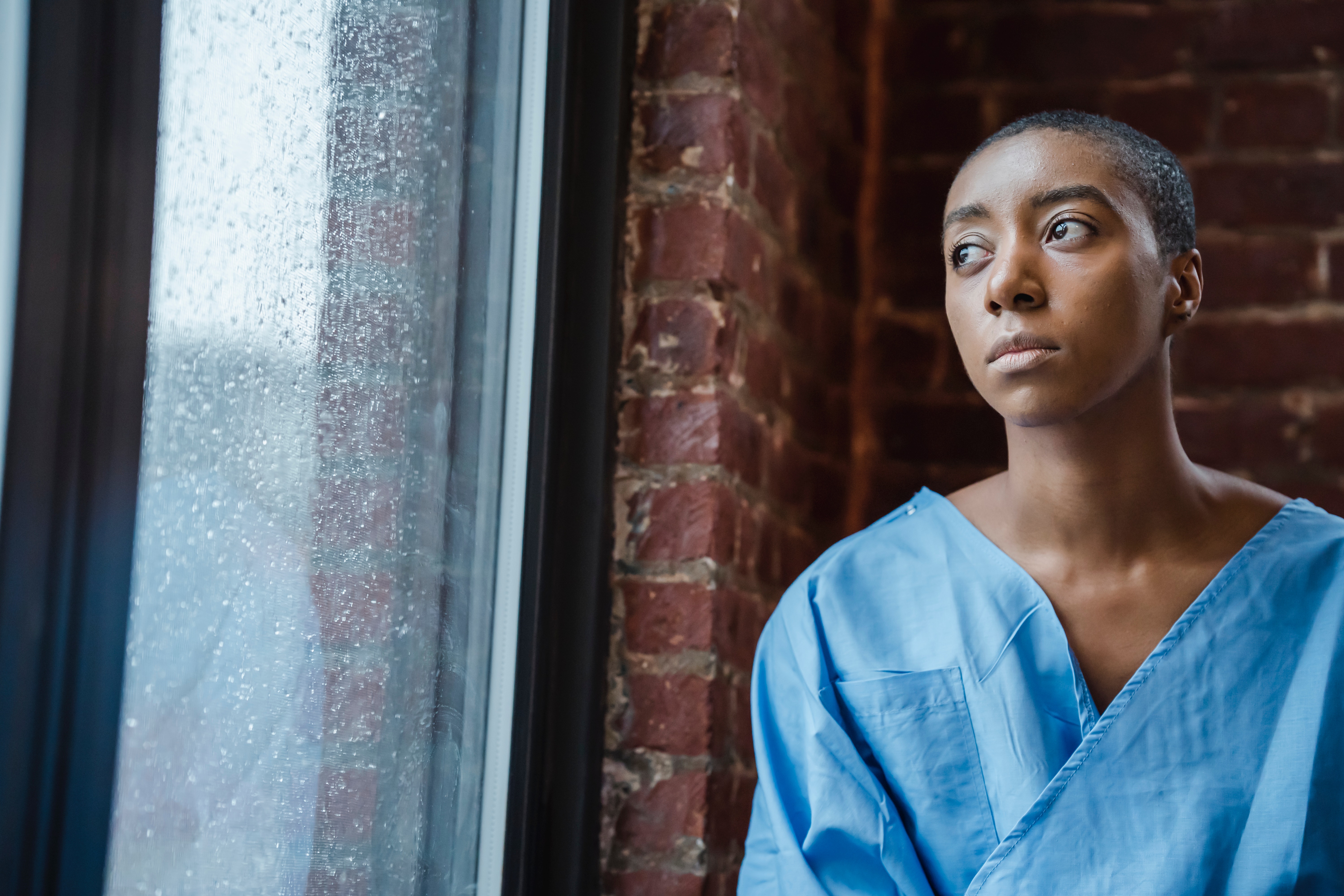 Picture of a Black woman in a hospital gown looking out of a window.